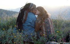 two people are sitting in the grass with their heads close to each other and kissing