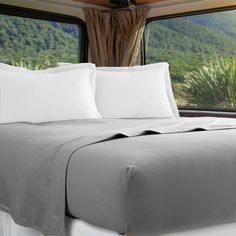 a bed with white sheets and pillows in front of a window overlooking the mountain range