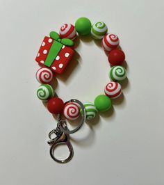 a red and green beaded bracelet with a christmas present on the clasp is sitting on a white surface