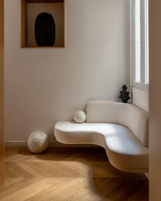 a white couch sitting under a window next to a wooden shelf filled with vases