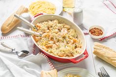 a red casserole dish filled with pasta and shrimp on a white tablecloth