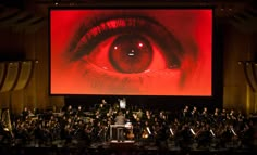 a large screen with an eye on it and orchestra members in front of the stage