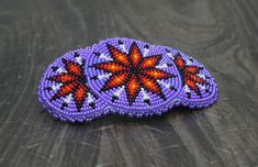 an orange and purple beaded brooch sitting on top of a wooden table