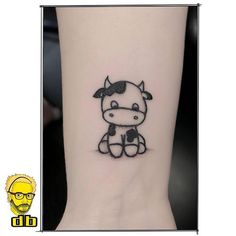 a small black and white cow tattoo on the ankle, next to a cartoon character