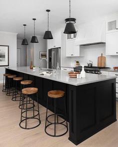 a kitchen with white cabinets and black counter tops, stools in front of the island