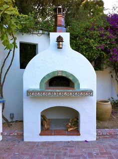 an outdoor pizza oven in the middle of a brick patio with potted plants on either side