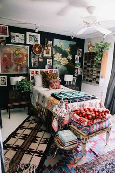 a bedroom with many pictures on the wall and a bed covered in pillows, blankets, and other items