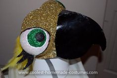 the head of a mannequin wearing a gold and black hat with green eyes