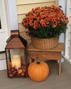 a basket full of flowers sitting next to a lantern and pumpkins on the porch