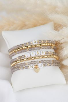 three bracelets with personalized charms on them sitting on top of a white pillow