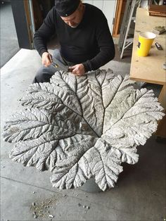 a man sitting on the ground working on a piece of art that looks like a leaf