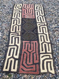 a black and red rug sitting on top of a gravel covered ground next to rocks