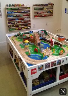 a toy train table in a playroom with toys on the floor and shelves behind it