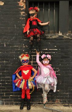 three children dressed up as superheros standing in front of a brick wall and window