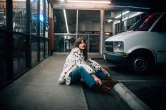 a woman sitting on the ground next to a white van in a parking lot at night