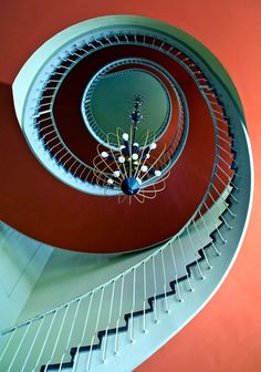 a spiral staircase with chandelier hanging from it's center point in an orange and red room