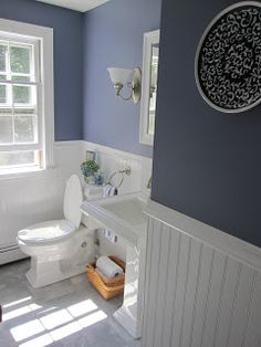 a white toilet sitting next to a sink in a bathroom under a window with blue walls