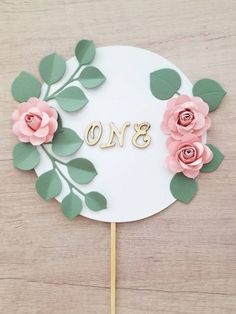 a cake topper with flowers and the number one on it, sitting on a wooden table