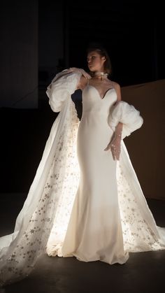 a woman in a white dress with a long veil on her head and hands behind her back