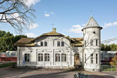 an old white house with a tower on the top and two cars parked in front