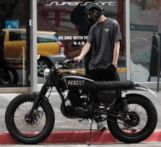 a man wearing a helmet standing next to a motorcycle parked on the side of a street