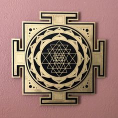 a golden and black wall hanging on the side of a pink wall with an intricate design