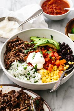 a white bowl filled with meat, rice and veggies next to two bowls of salsa