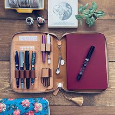 the contents of a travel case are laid out on a wooden table, including pens and pencils