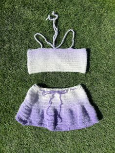 two pieces of knitted clothing laying on top of the grass, one in purple and white