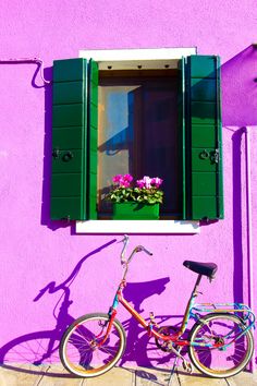 a bike parked in front of a purple building with green shutters and flowers on the window sill