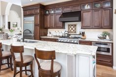 a large kitchen with wooden cabinets and marble counter tops, along with bar stools