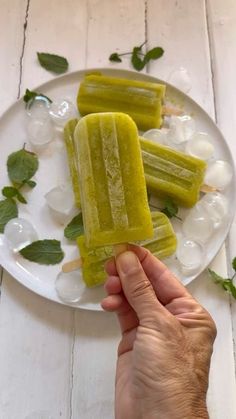 a person is holding a popsicle on a plate with ice cubes and mint leaves