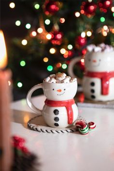 two snowman mugs sitting on top of a table next to a christmas tree