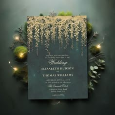 an elegant wedding card with gold foil on it and greenery in the background, surrounded by lights