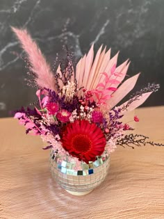 a vase filled with pink and purple flowers on top of a wooden table next to a mirror ball