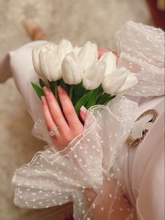 a woman in white dress holding a bouquet of white tulips on her hand