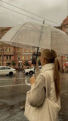 a woman holding an umbrella in the rain on a city street with cars behind her