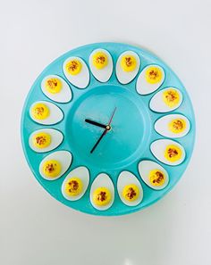 a clock made out of hard boiled eggs on a blue plate with black hands and feet