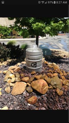 a trash can sitting on top of a pile of rocks next to a green tree