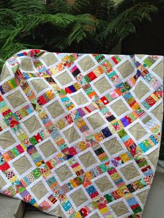 a quilted blanket sitting on top of a wooden bench next to a planter