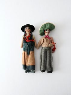 two dolls are standing next to each other on a white surface, one is wearing a hat and the other has a scarf around his neck