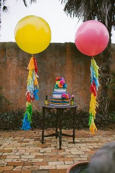 a table topped with cake and balloons next to a brick wall covered in palm trees