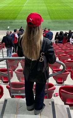 a woman with long hair wearing a red hat stands in front of a stadium full of empty seats