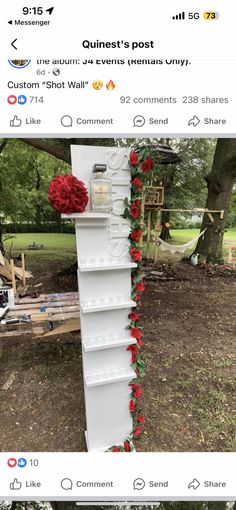 a tall white shelf with red flowers on the top and bottom, sitting in front of a tree