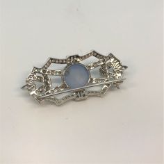 A Ladies Platinum 1 3/4 Inch Long Antique Brooch Set With A 12 Mm Round Natural Blue Grey Star Sapphire Weighing Approximately 10 Carats. The Brooch Is Also Set With 104 Round Diamonds And 6 Marquise Cut Diamonds Having A Combined Weight Of Approximately 1.33 Carats. Blue Diamond Gemstone Brooches, Vintage Blue Diamond Brooch, Vintage Blue Diamond Brooches, Blue Hallmarked Brooches For Anniversary, Collectible Hallmarked Blue Brooches, Blue Cabochon Brooch For Formal Occasions, Formal Blue Gemstone Brooch, Formal Blue Cabochon Brooch, Formal Blue Gemstone Brooches