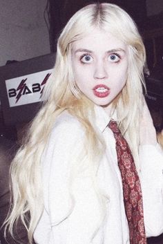 a woman with pink hair wearing a white shirt and tie is posing for the camera