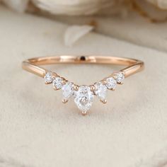 a rose gold ring with three pear shaped diamonds on the top and bottom, in front of a white flower