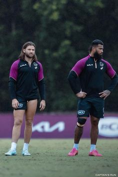 two men in black and pink uniforms standing on the field with their hands behind their backs