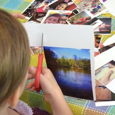 a child is holding a red pen and looking at pictures on the table with them