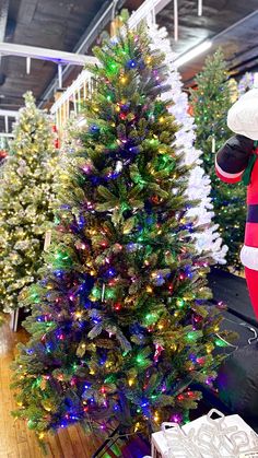 santa clause standing next to a christmas tree in a room filled with other christmas trees